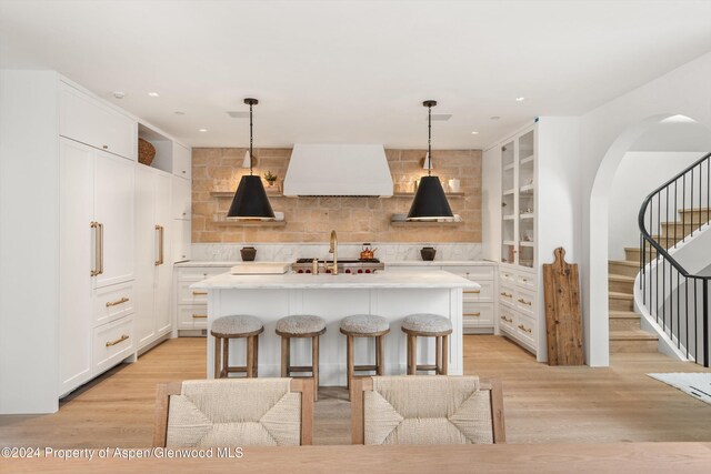 kitchen featuring white cabinets, decorative light fixtures, a kitchen island with sink, and custom exhaust hood