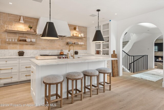 kitchen with light stone counters, white cabinetry, hanging light fixtures, and a kitchen island with sink