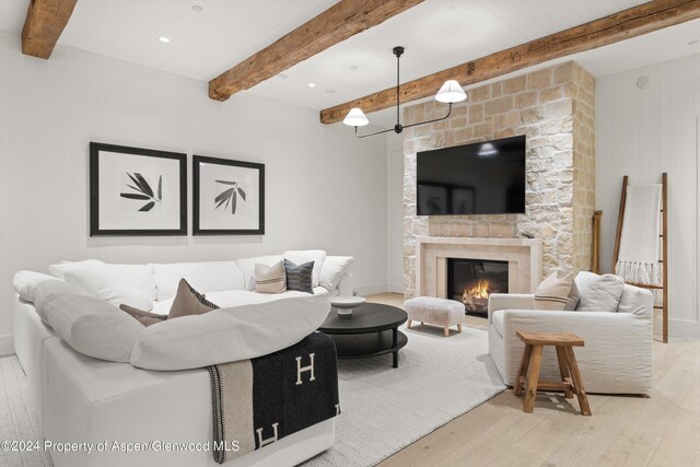 living room with beam ceiling, a stone fireplace, and light hardwood / wood-style flooring