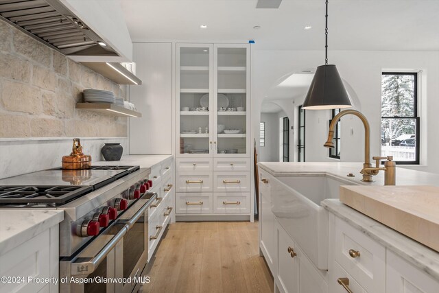 kitchen featuring light wood-type flooring, high end stove, exhaust hood, pendant lighting, and white cabinetry