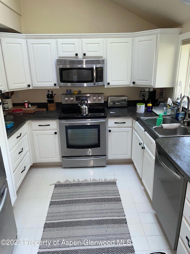 kitchen with white cabinets, sink, vaulted ceiling, light tile patterned floors, and appliances with stainless steel finishes