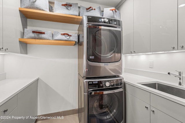 clothes washing area with stacked washer and dryer, sink, and cabinets