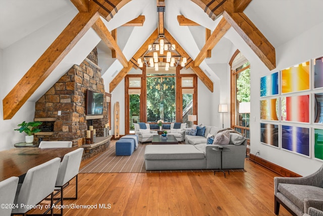 living room featuring a notable chandelier, light hardwood / wood-style floors, beamed ceiling, a stone fireplace, and high vaulted ceiling