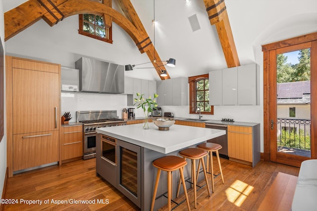 kitchen with wall chimney range hood, a kitchen island, sink, white cabinets, and beverage cooler