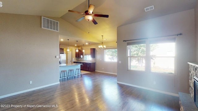 unfurnished living room with ceiling fan with notable chandelier, dark wood-type flooring, high vaulted ceiling, and a brick fireplace