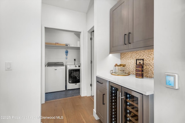 bar with washing machine and dryer, decorative backsplash, light hardwood / wood-style flooring, and beverage cooler