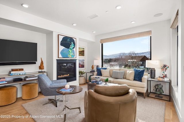 living area with a glass covered fireplace, recessed lighting, a mountain view, and wood finished floors