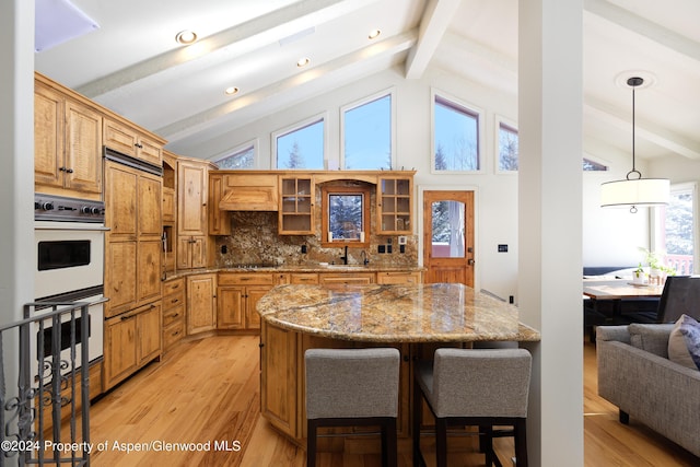 kitchen featuring lofted ceiling with beams, light wood-type flooring, backsplash, and double oven