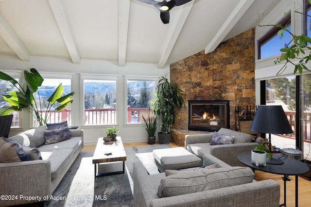 sunroom with vaulted ceiling with beams, ceiling fan, and a stone fireplace