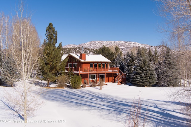 snow covered rear of property with a deck with mountain view