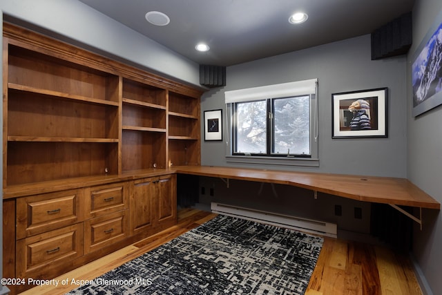 office area with light wood-type flooring, built in desk, and a baseboard heating unit