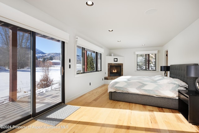 bedroom featuring access to exterior, hardwood / wood-style floors, a tiled fireplace, and a mountain view