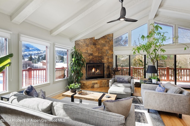 sunroom / solarium with a stone fireplace, ceiling fan, a mountain view, and lofted ceiling with beams