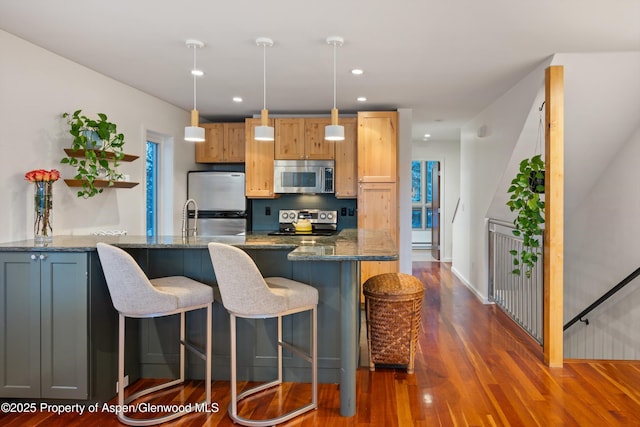 kitchen featuring a breakfast bar area, appliances with stainless steel finishes, dark stone counters, and dark wood-style flooring