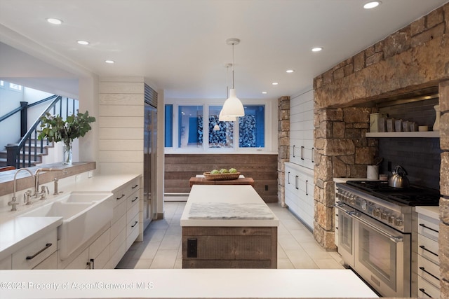 kitchen with light tile patterned floors, range with two ovens, pendant lighting, white cabinets, and sink