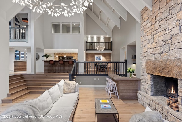 living room featuring a stone fireplace, a notable chandelier, high vaulted ceiling, light hardwood / wood-style flooring, and beam ceiling