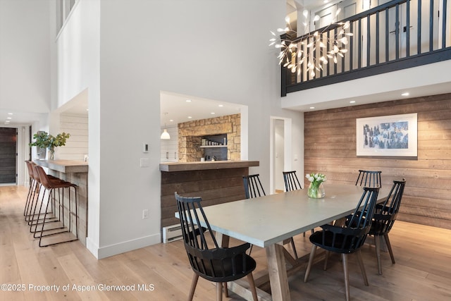 dining room with light hardwood / wood-style floors, a high ceiling, wood walls, and an inviting chandelier