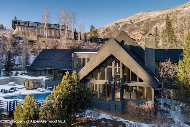 snow covered back of property featuring a mountain view and a fenced in pool