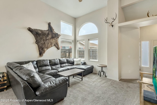 carpeted living area featuring ceiling fan, a high ceiling, and baseboards