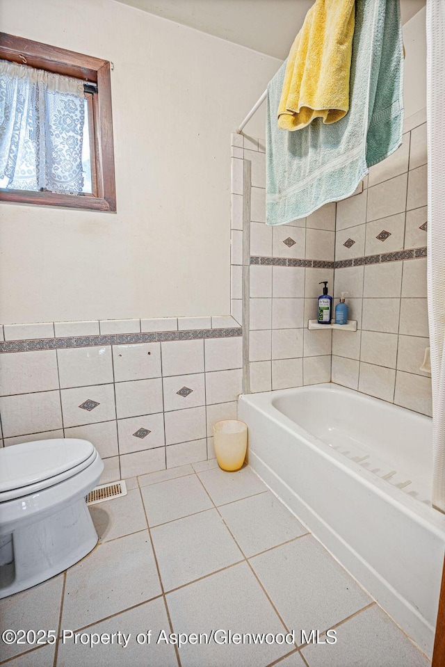 full bath with bathtub / shower combination, toilet, tile patterned flooring, tile walls, and wainscoting