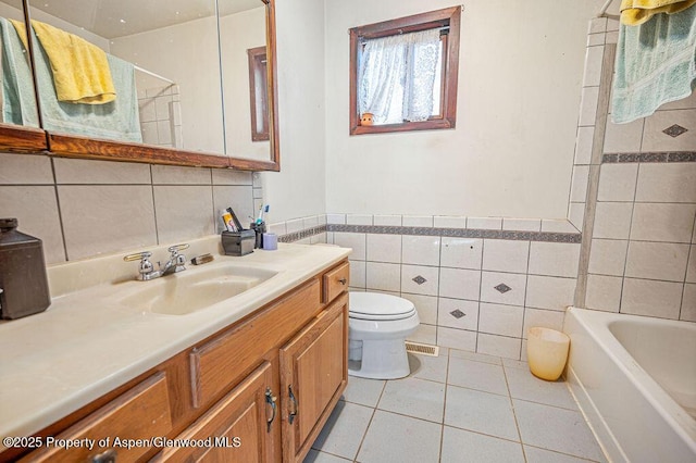 full bath with toilet, a wainscoted wall, tile patterned floors, vanity, and tile walls