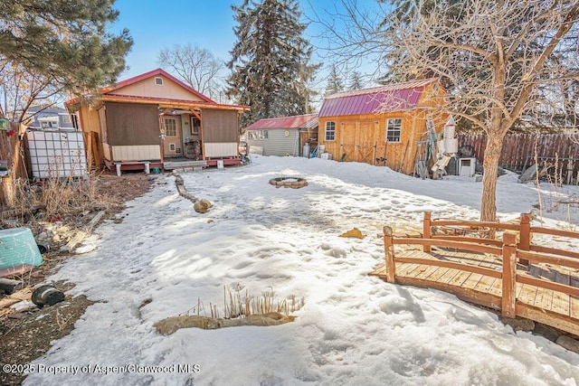 snow covered rear of property featuring an outdoor structure and fence