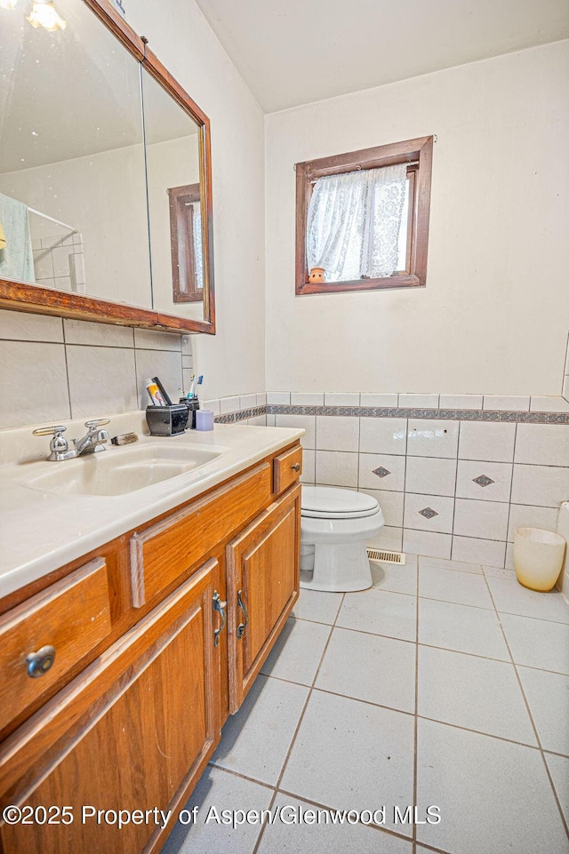 bathroom with wainscoting, toilet, tile patterned flooring, vanity, and tile walls