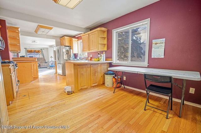 kitchen featuring light wood-style flooring, a peninsula, stainless steel appliances, open shelves, and a sink