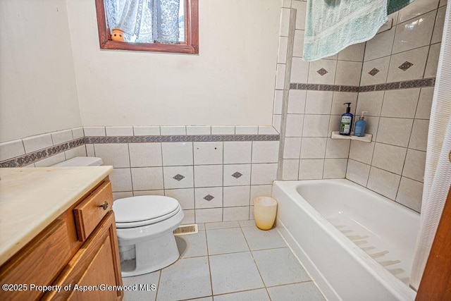 bathroom with toilet, visible vents, vanity, tile walls, and tile patterned floors