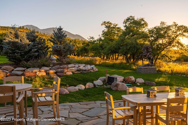 patio terrace at dusk featuring a mountain view and a yard