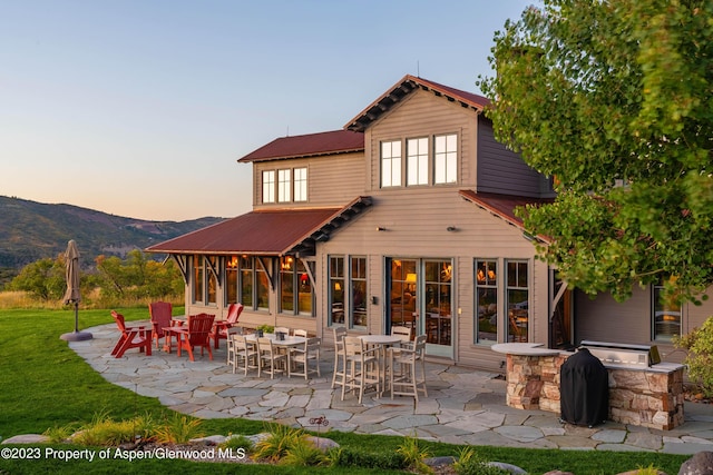 back house at dusk with a lawn, a mountain view, and a patio area