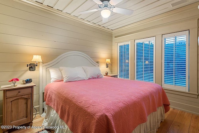 bedroom with wood walls, ceiling fan, and light hardwood / wood-style floors