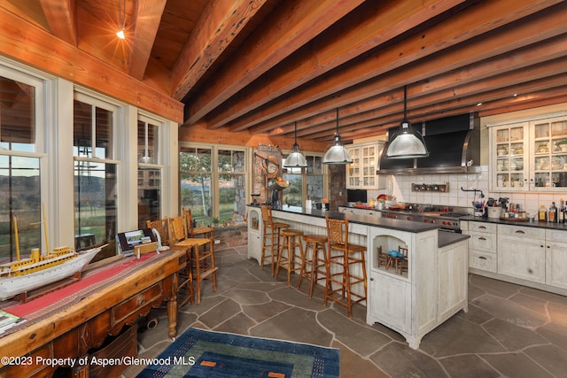 kitchen with tasteful backsplash, wall chimney range hood, decorative light fixtures, beamed ceiling, and white cabinets