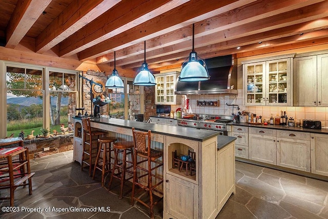 bar with ventilation hood, hanging light fixtures, decorative backsplash, high end stove, and cream cabinetry