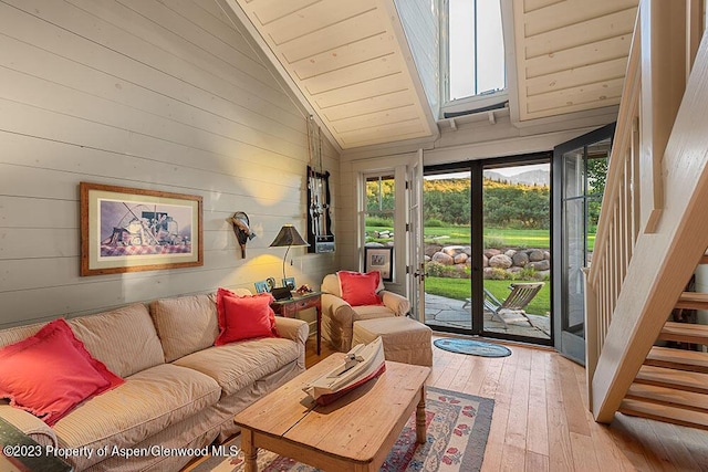 living room with wooden walls, light hardwood / wood-style flooring, high vaulted ceiling, and a healthy amount of sunlight