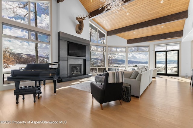 living area featuring high vaulted ceiling, wooden ceiling, wood finished floors, beamed ceiling, and a glass covered fireplace