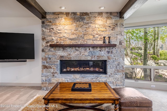 carpeted living room with a stone fireplace, beamed ceiling, and baseboards