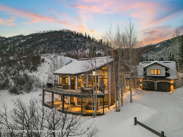 snow covered back of property with a garage, stone siding, and a mountain view