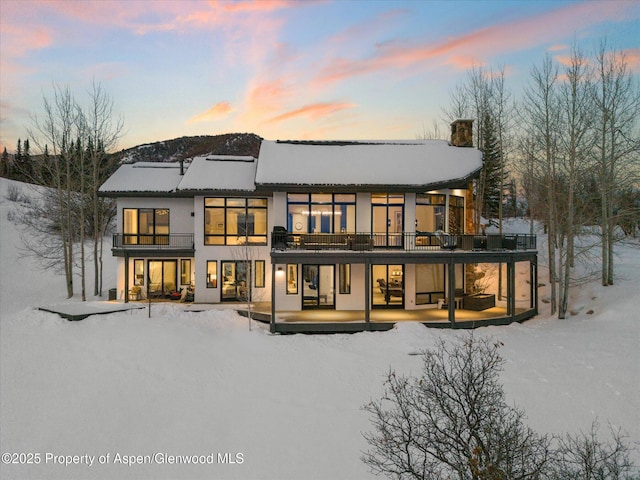 snow covered house featuring a patio area, a balcony, and stucco siding