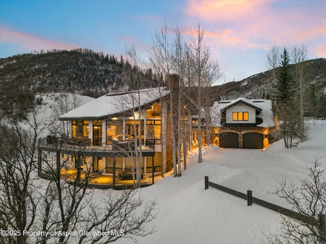 36125 Quarry Ridge Rd, Steamboat, CO 80487 - snow covered back of property featuring a chimney, a mountain view, an attached garage, and stone siding