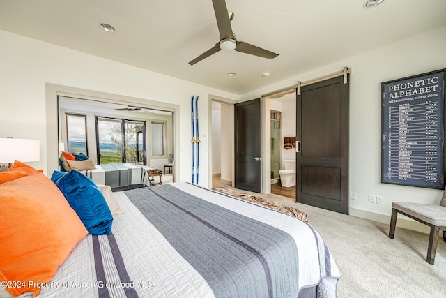 carpeted bedroom with access to exterior, a barn door, ceiling fan, ensuite bath, and baseboards