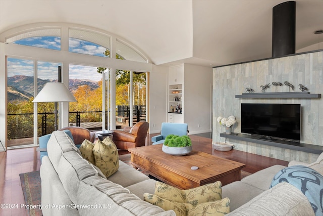 living room with built in shelves, a mountain view, wood-type flooring, and vaulted ceiling