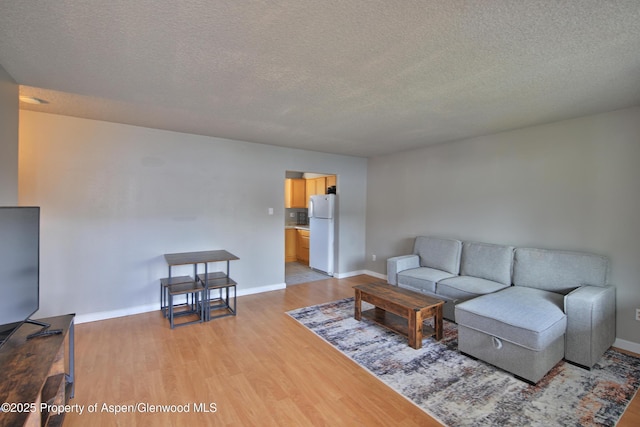 living area with light wood finished floors, a textured ceiling, and baseboards