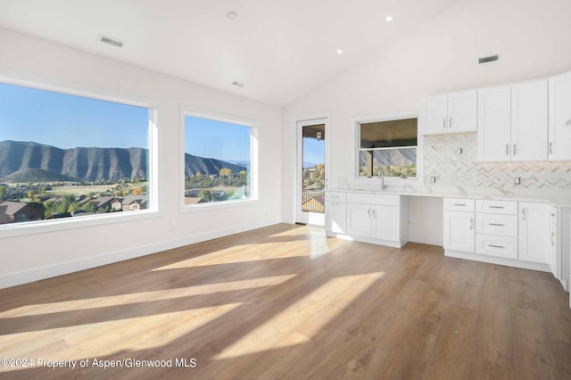 kitchen featuring decorative backsplash, light wood-type flooring, white cabinets, vaulted ceiling, and a mountain view