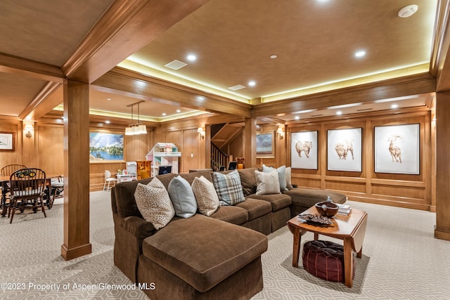 carpeted living room featuring crown molding, wooden walls, and decorative columns