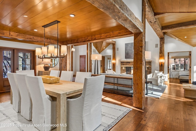 dining area featuring lofted ceiling with beams, wooden ceiling, hardwood / wood-style floors, a stone fireplace, and plenty of natural light