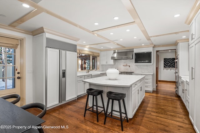 kitchen with white cabinets, paneled fridge, and wall chimney range hood