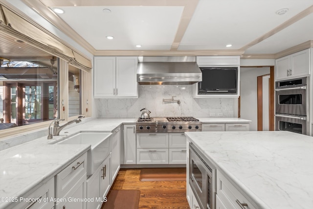 kitchen with backsplash, wall chimney exhaust hood, stainless steel appliances, hardwood / wood-style flooring, and white cabinets