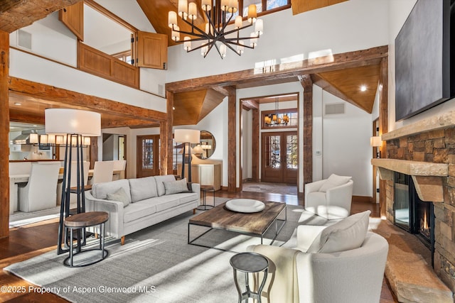 living room featuring a stone fireplace, french doors, high vaulted ceiling, and an inviting chandelier