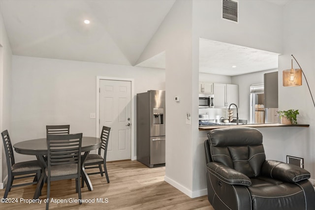 dining room featuring light hardwood / wood-style floors, lofted ceiling, and sink